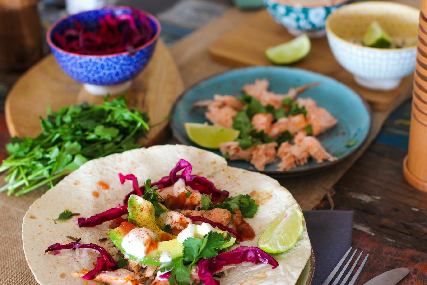 A fresh salmon taco with avocado, red cabbage, and lime on a rustic table